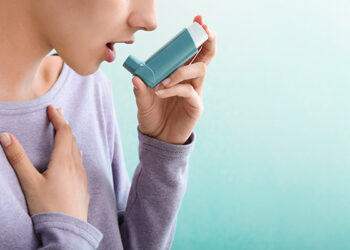 Young woman using inhaler against asthma on color background