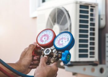 Air repair mechanic using measuring pressure gauge equipment for filling home air conditioner after cleaners and checking maintenance outdoor air compressor unit.