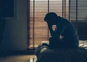 Sad businessman sitting head in hands on the bed in the dark bedroom with low light environment