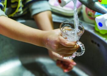 Close-up of the hands of a little boy filling a glass of water on the tap. Shallow depth of focus.