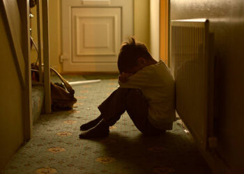 sad child with his head between his legs left alone at home