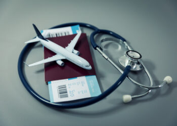 travel insurance - passport with flight ticket and stethoscope on gray background