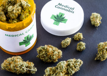 Medical marijuana buds in large prescription bottle with branded cap on black background