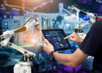 Hands holding tablet on blurred automation machine as background